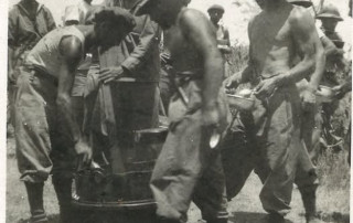 Fotografia d'epoca di soldati del Regio Esercito in Africa con casco coloniale intorno a una cucina da campo.